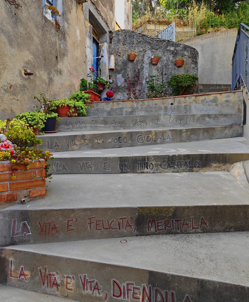 Scalinata decorata nel borgo di Simeri Crichi con frasi sulla vita e vasi di fiori lungo il percorso